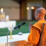 Buddhist monk meditating with hands folded, candle glowing nearby